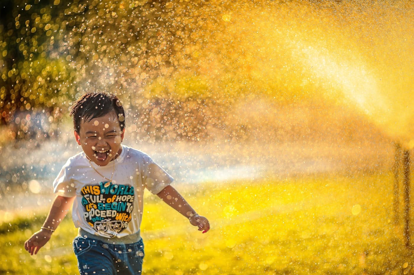 A young boy running through a sprinkler